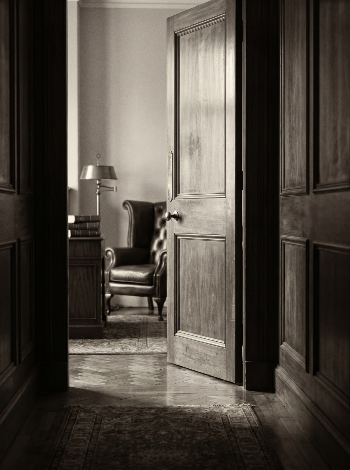 Editorial detail of a panelled walnut door half-open onto an empty chambers room. Sample placeholder.